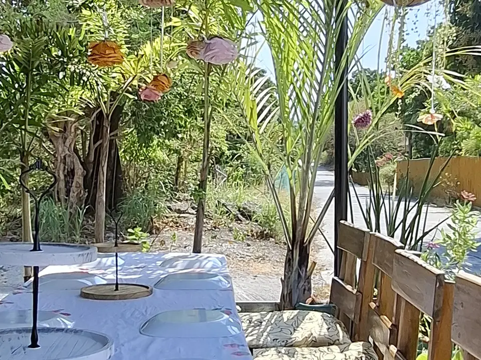 Kape Parola's long garden table set for tea under a bamboo roof, with the sea beyond the lighthouse road